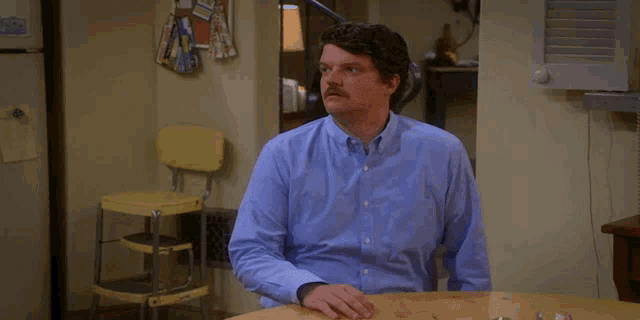 a man in a blue shirt sits at a table in front of a refrigerator that says ' smith ' on it