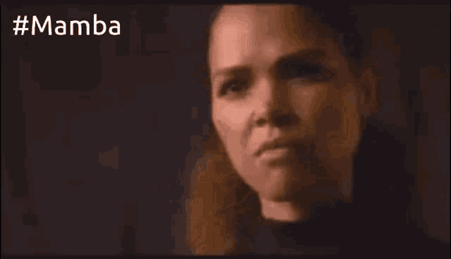a close up of a woman 's face in a dark room with the words mamba behind her .