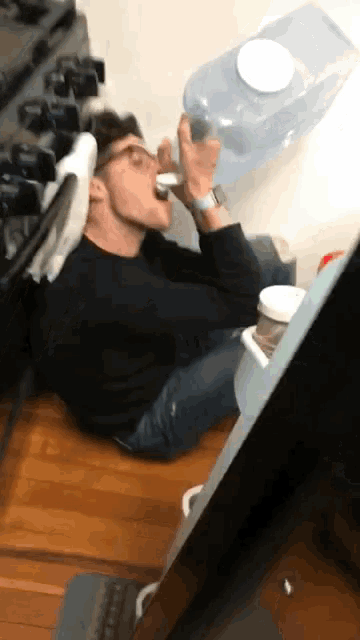 a man is drinking from a bottle while laying on the floor