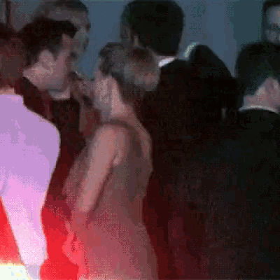 a group of people are standing in a dark room and one of them is wearing a red dress
