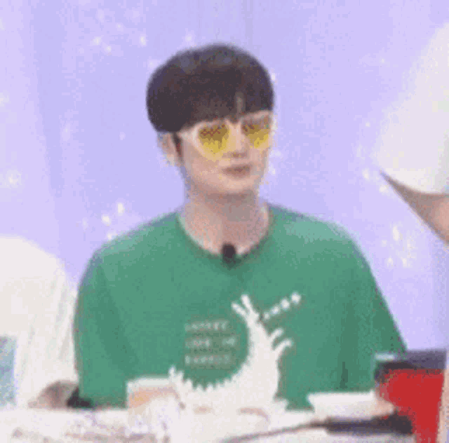 a young man wearing a green shirt and yellow sunglasses is sitting at a table .