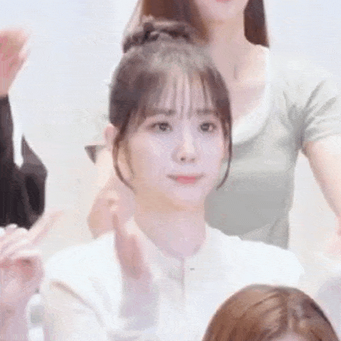 a woman in a white shirt is sitting in front of a group of people and making a peace sign .
