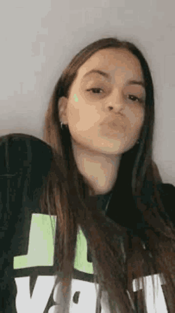 a young woman with long hair is blowing a kiss while wearing a black and green shirt .