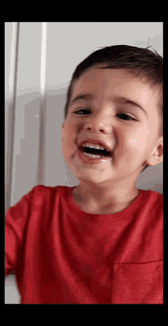 a young boy in a red shirt is smiling with a black toothbrush in his mouth