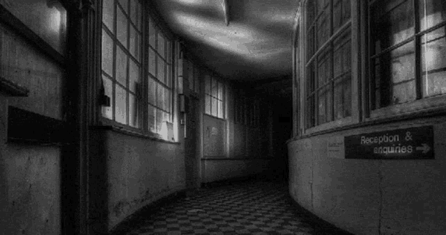 a black and white photo of a hallway with a sign pointing to the reception and enquiries