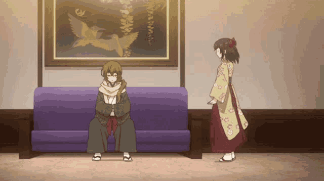 a man sits on a purple couch while a woman stands next to him