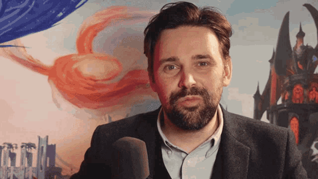 a man with a beard stands in front of a microphone with a painting in the background