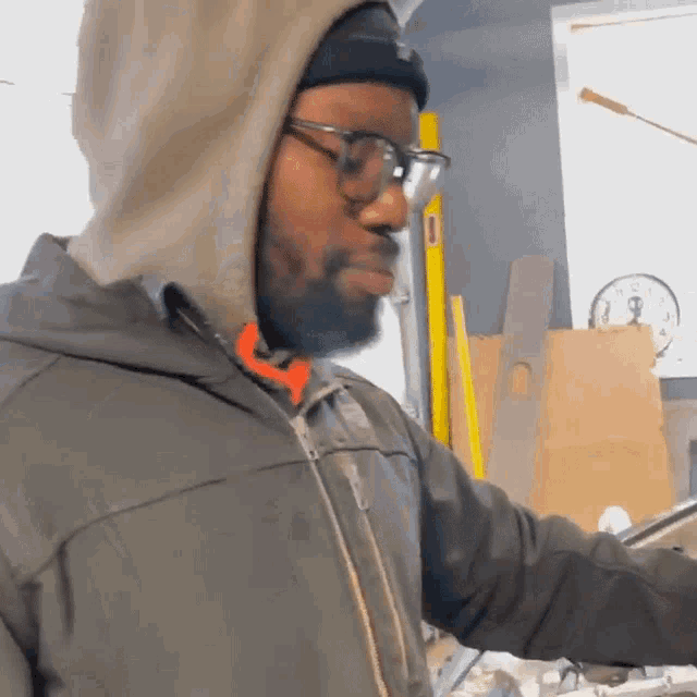 a man wearing glasses and a hooded jacket is standing in front of a clock that says 4:20