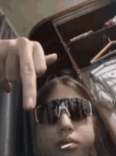 a woman wearing sunglasses is smoking a cigarette and giving a middle finger .