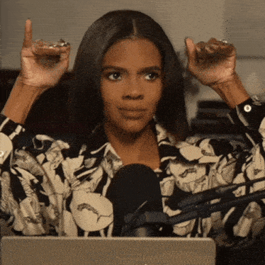 a woman in a floral shirt is sitting in front of a microphone with her hands in the air