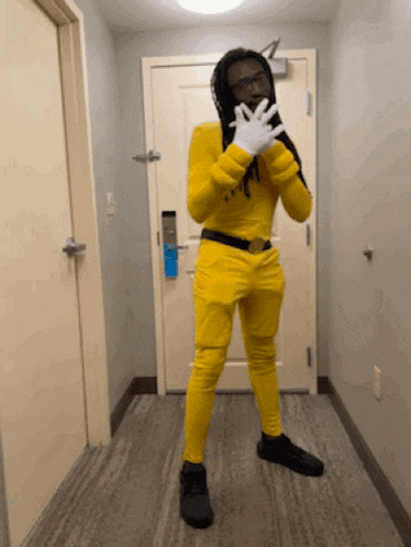 a man in a yellow suit and white gloves stands in a hallway