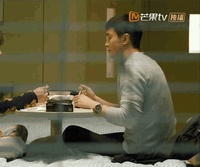 a man sits at a table with a box of tissues in front of him with a tv logo in the corner