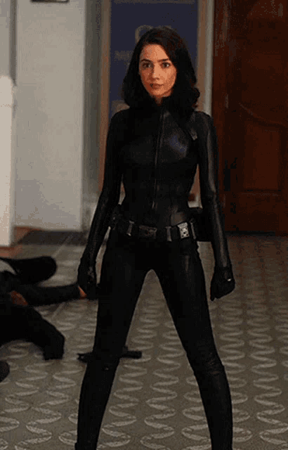 a woman in a black jumpsuit is standing in a hallway