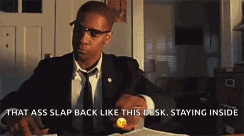 a man in a suit and tie is sitting at a desk and saying that ass slap back like this desk staying inside .