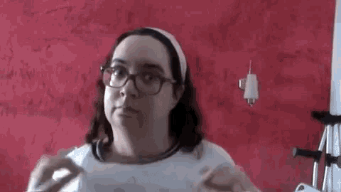 a woman wearing glasses and a headband is standing in front of a red wall with graffiti on it .