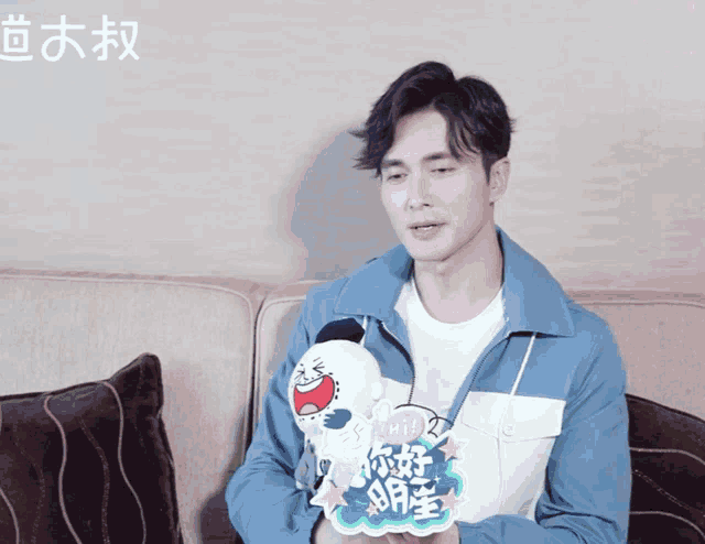 a man sitting on a couch holding a stuffed animal that says " hi " on it