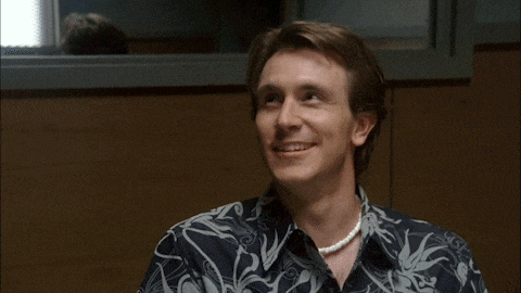 a man wearing a pearl necklace and a hawaiian shirt smiles