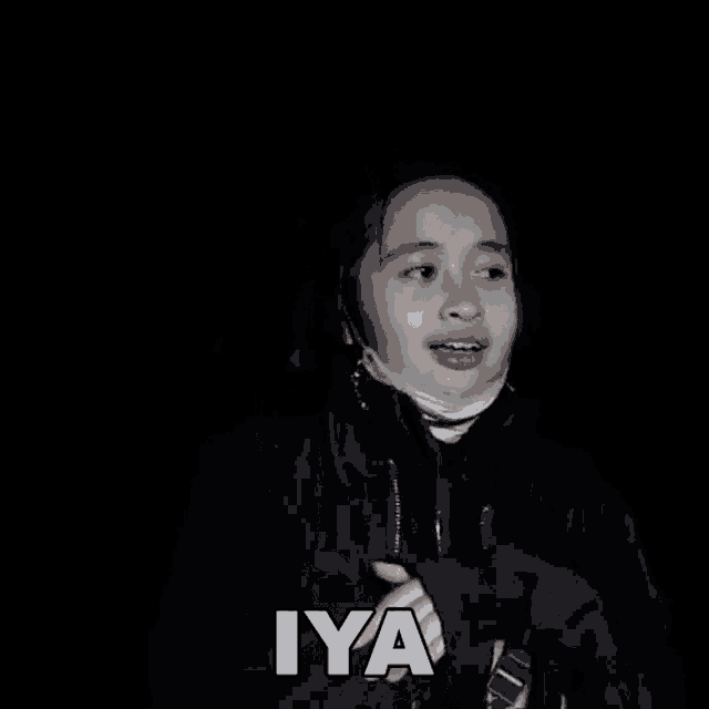 a young girl wearing a mask and a black jacket is making a funny face and saying iya .