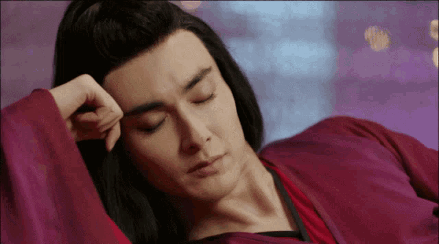 a man with long hair is laying down with his hand on his head