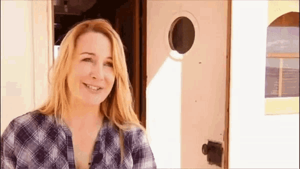 a woman in a plaid shirt is smiling in front of a window