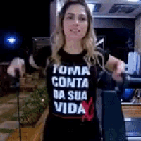 a woman wearing a black t-shirt that says toma conta da sua vida is standing in a kitchen .
