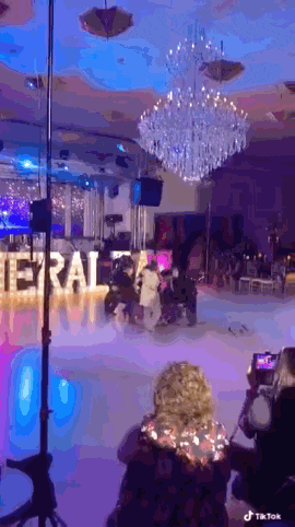 a woman is taking a picture of a group of people dancing in a large room .