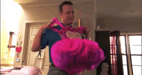 a man in a blue shirt is holding up a pink dress