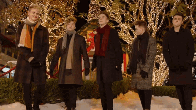 a group of young men are standing in front of a christmas tree