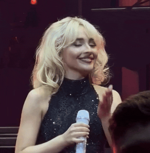 a blonde woman in a black dress is holding a microphone and smiling
