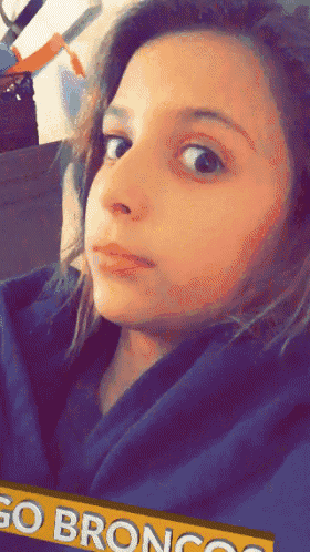 a young girl is wearing a blue hoodie with a go broncos banner in the background