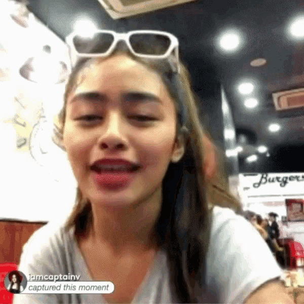 a woman wearing sunglasses is sitting in front of a sign that says burgers on it