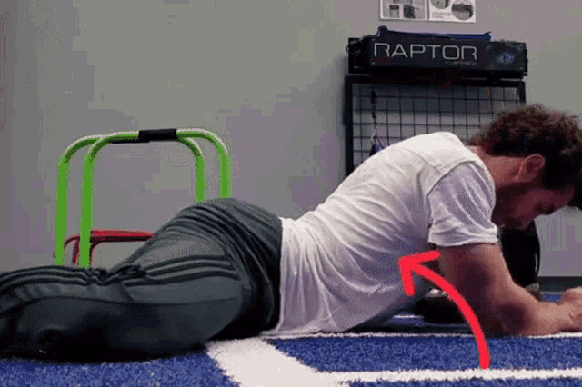 a man is doing a plank on the floor in front of a raptor sign