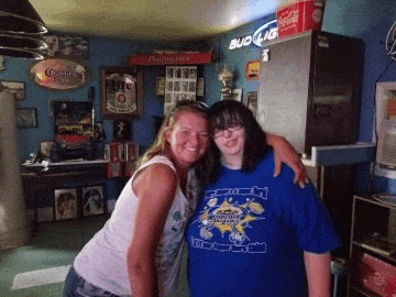 two women are posing for a picture in a room with a budweiser sign on the wall .