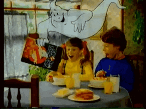 a boy and a girl are sitting at a table with a box of ghostbusters cereal