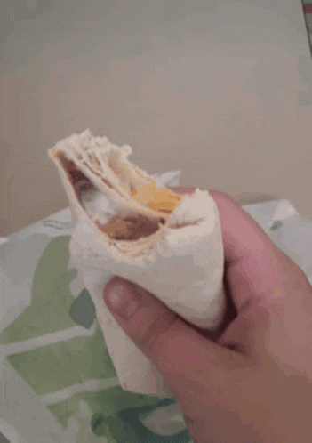 a person is holding a tortilla that has been cut in half and covered in sauce