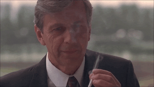 a man in a suit smoking a cigarette with smoke coming out of his mouth