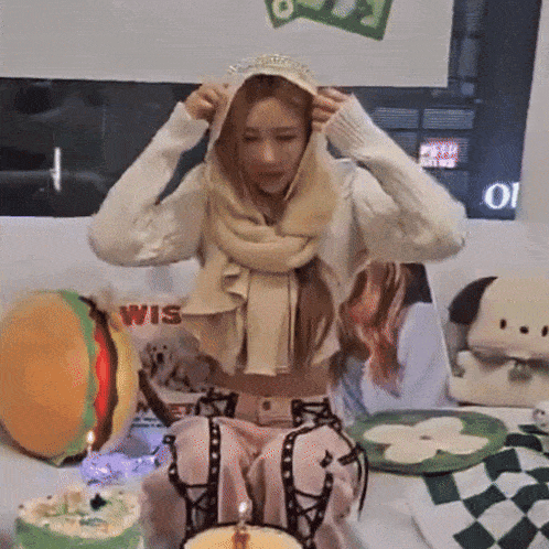 a woman wearing a scarf and a crown is sitting in front of a cake