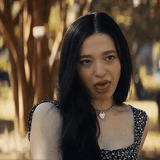 a woman with long black hair is making a funny face while wearing a necklace .