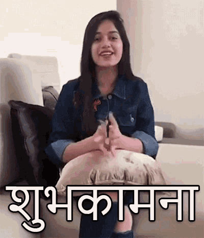 a woman is sitting on a couch with a pillow and a sign that says ' shubh kamana ' on it