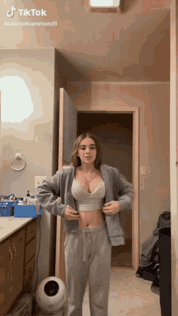 a woman in a crop top and sweatpants is standing in a bathroom ..