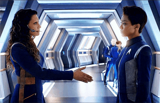 two women are shaking hands in a hallway while wearing blue uniforms
