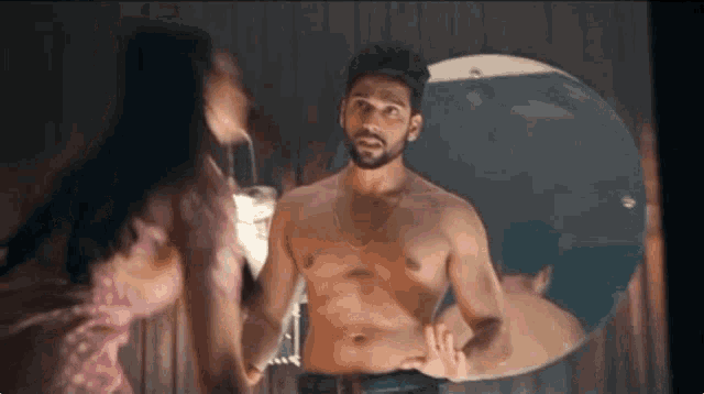 a man without a shirt is standing in front of a mirror with a woman .
