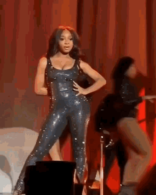 a woman in a black jumpsuit is standing on a stage with her hands on her hips .