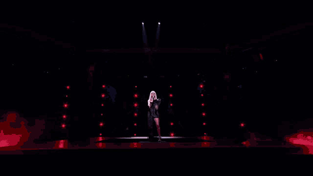 a woman singing on a stage with a group of dancers behind her