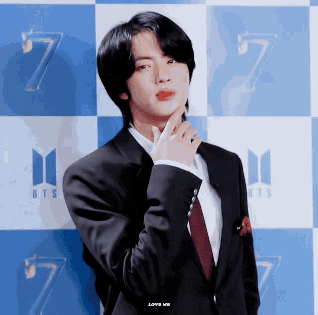 a man in a suit is standing in front of a blue and white checkered background with the number 7 on it