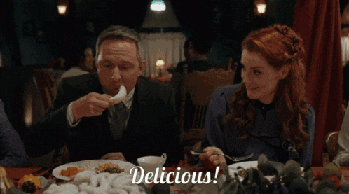 a man and a woman are sitting at a table with a plate of food and the word delicious on the bottom right