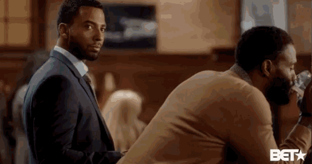 a man in a suit and tie is standing next to another man in a bar .