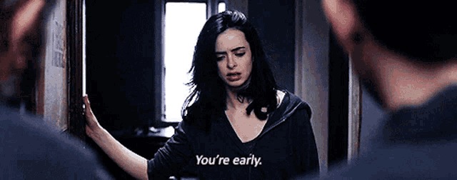 a woman is standing in a hallway talking to a man and says `` you 're early '' .