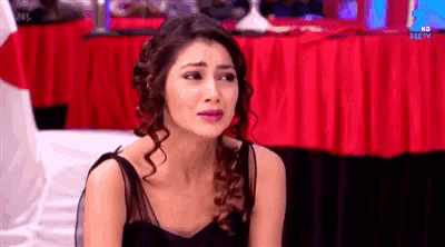 a woman in a black dress is sitting on the floor in front of a red curtain .