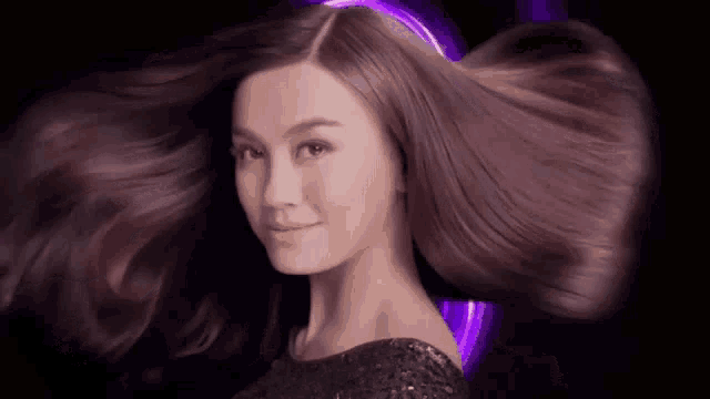 a woman with long hair is standing in front of a purple background .